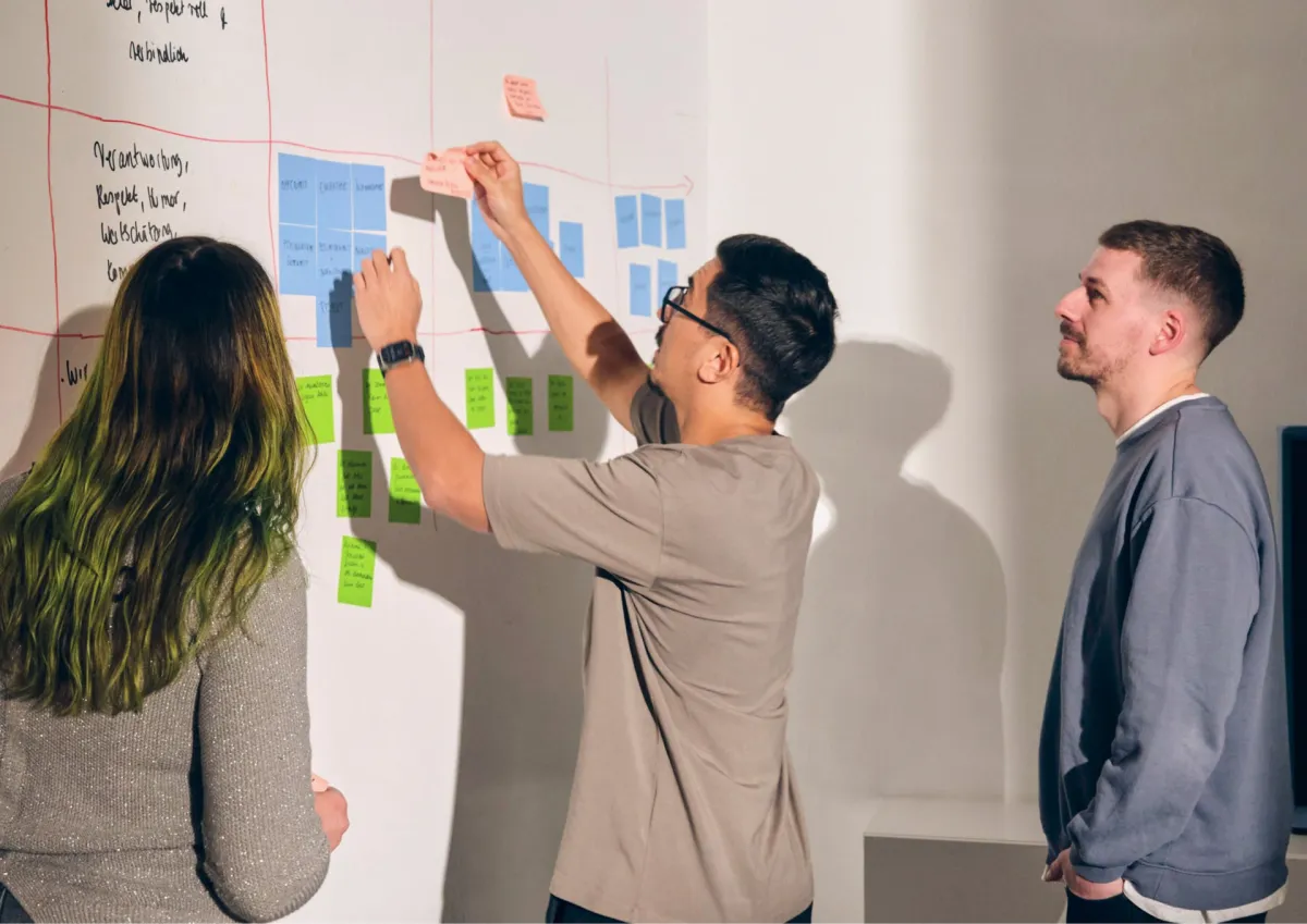 Three people standing and arranging sticky notes on a whiteboard during a team workshop