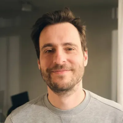 Person with short brown hair and a beard, wearing a grey sweatshirt indoors